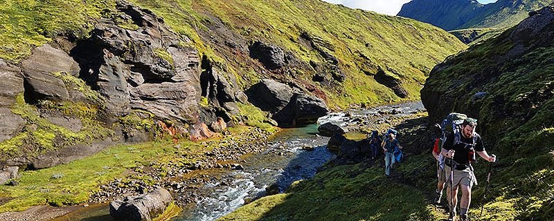 Hikers near river passing through grassy ravine