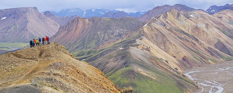 Distant hikers climbing grassy Icelandic mountains